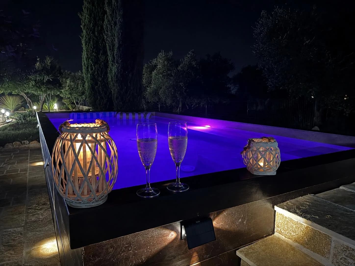 Piscina in cromoterapia viola con calici di champagne e lanterne accese, sera