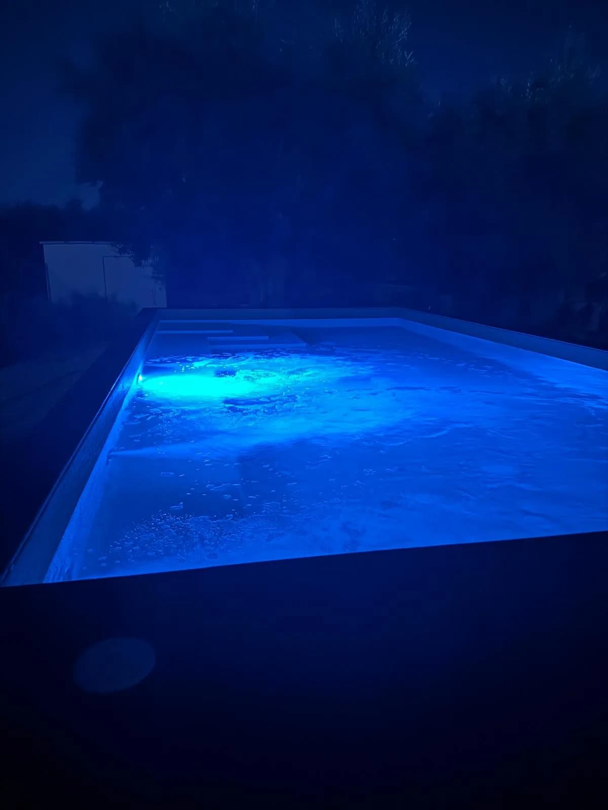 Piscina in cromoterapia blu di notte tra i cipressi